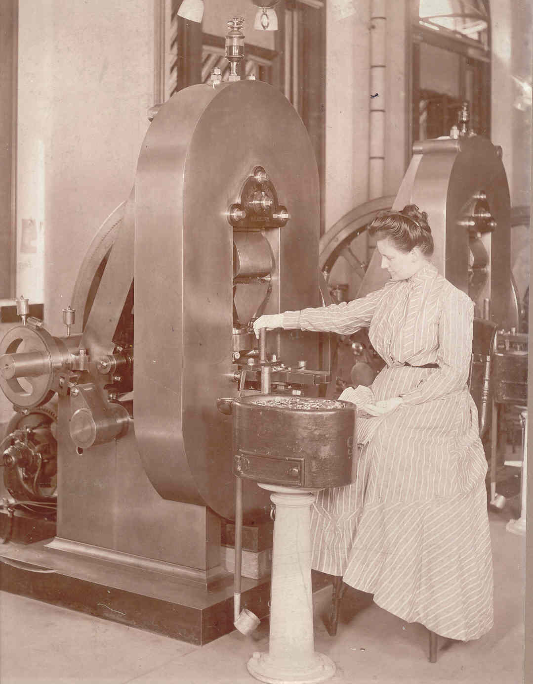 Woman sitting in front of a coin press feeding coins into a tube.